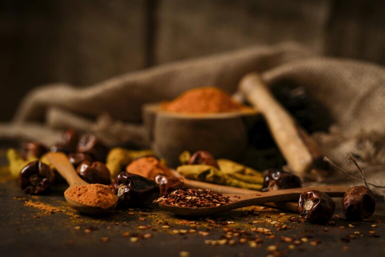 A close-up of rustic spices such as chilies and turmeric on wooden spoons, highlighting food textures.